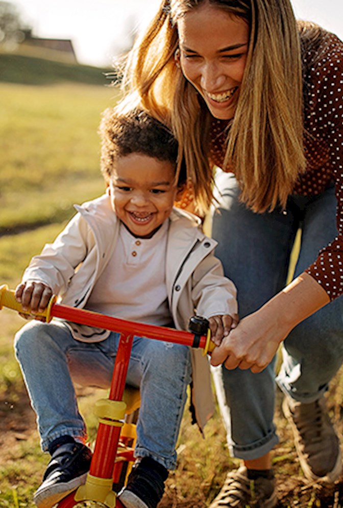 Woman outside with small child teaching him how to ride a bike