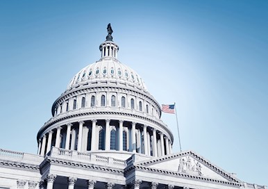 Outside view of US Capitol rotunda against blue sky with American flag waving on pole