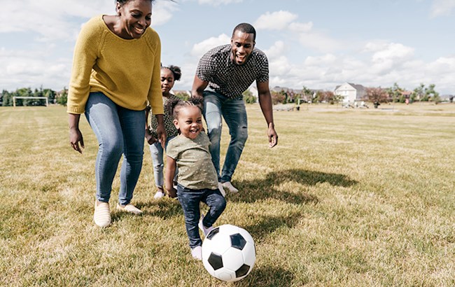 Parents with two small children playing soccer outside