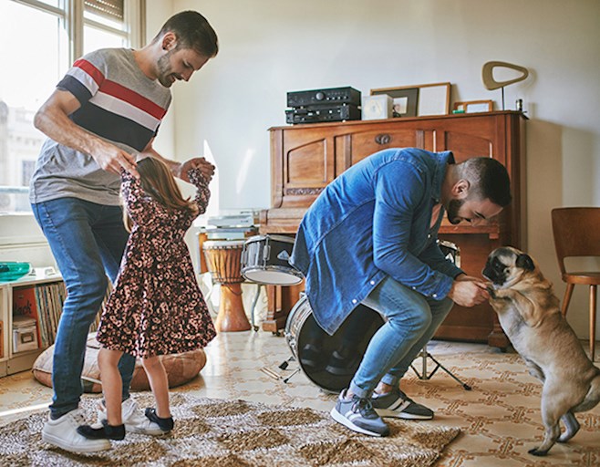 Parents dancing in living room with young girl and dog