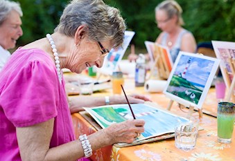 Three senior women outside at table painting lighthouses
