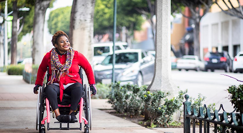 Woman smiling in wheelchair outside on city sidewalk