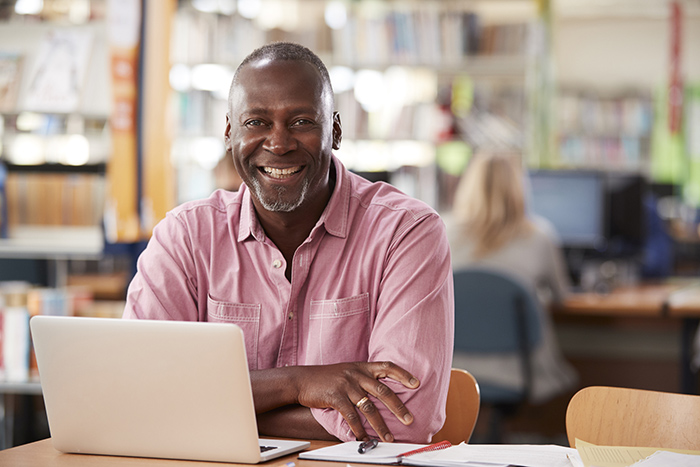 Smiling older man with open laptop looking at camera inside library