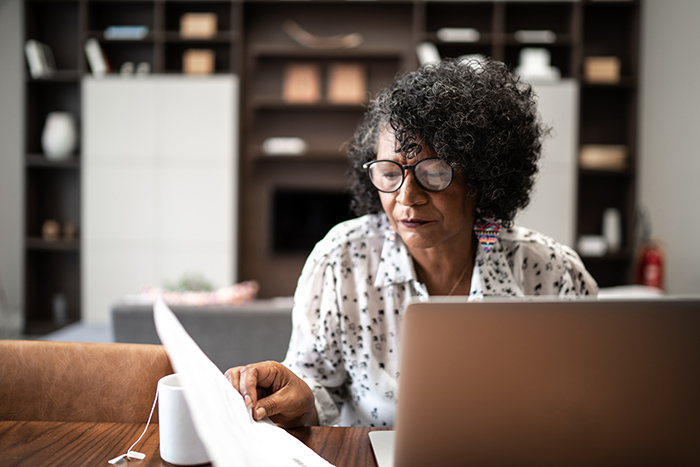 Older woman sitting at table with open laptop reading paperwork