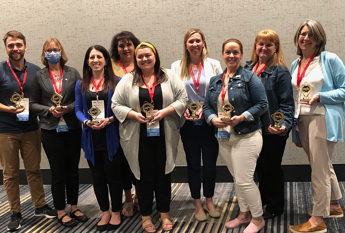 Nine people wearing AOTA INSPIRE badges with orange lanyards and holding small gold trophies. The trophies have the word "winner" written on the front. 