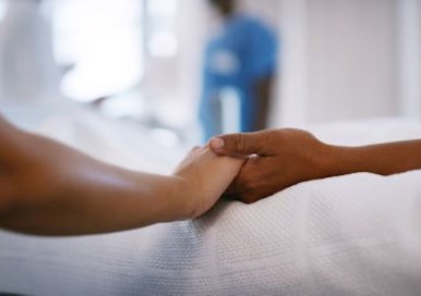 Image of someone holding hand of a person in a hospital bed