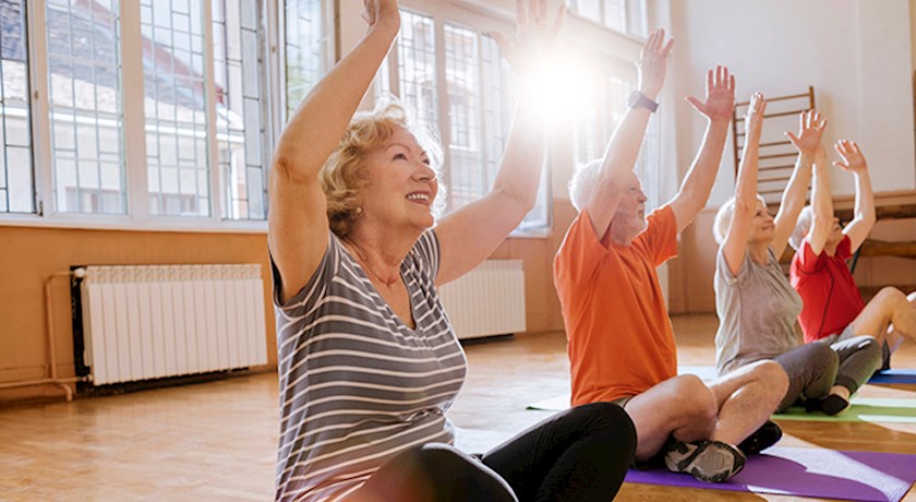 Group of seniors sitting on yoga mats with arms raised in the air