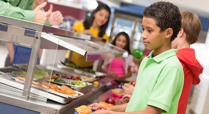 Boy in cafeteria line at school with classmates and a tray of food