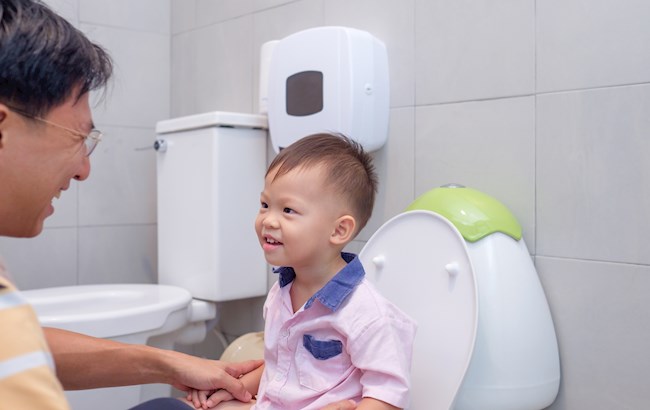 Toddler and adult in bathroom. Child sits on potty training seat.