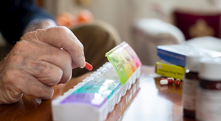 Close up of an elderly mans hands putting pills into pill case with other medication on table
