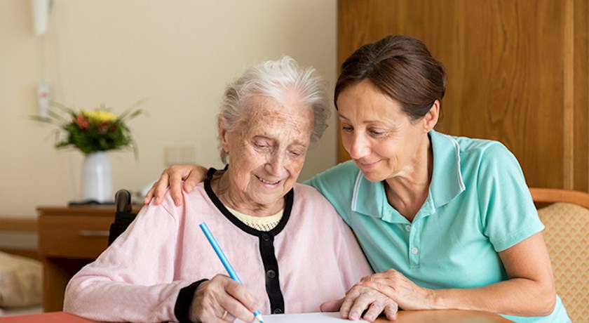 Female occupational therapist alongside senior woman holding a pencil working on handwriting skills