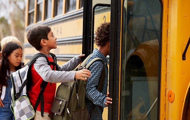 Three school aged kids wearing backpacks and entering school bus