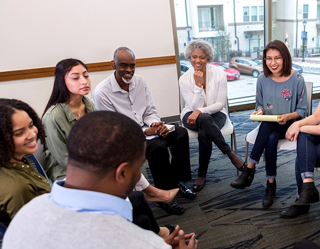 Diverse group of people sitting in a circle talking in chairs inside a room