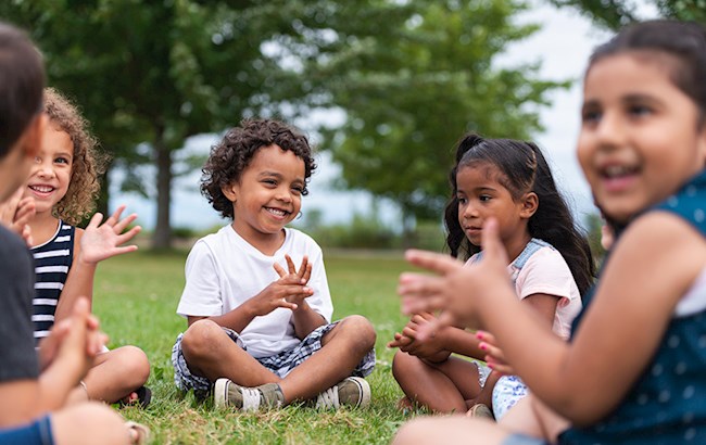 Diverse group of preschool kids sitting in circle outside laughing