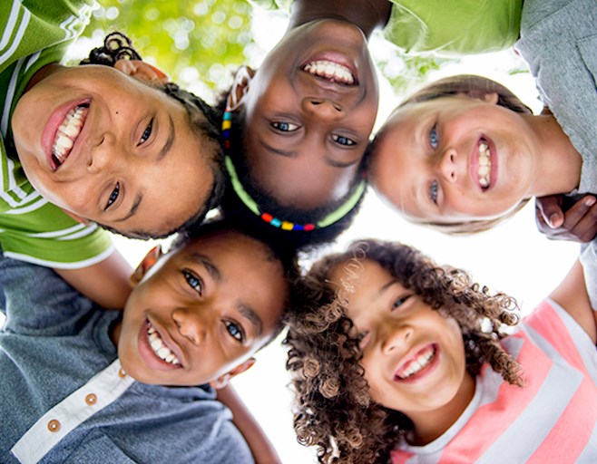 Diverse group of smiling kids with arms around each other looking down into camera