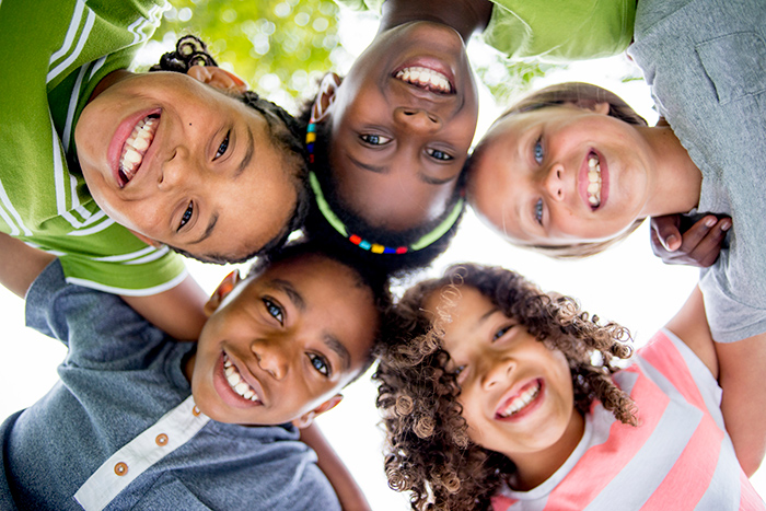 Diverse group of smiling kids with arms around each other looking down into camera