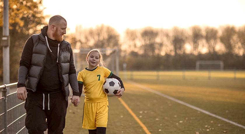 Father walking with daughter outside wearing soccer uniform and holding soccer ball