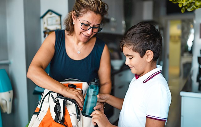 Mother helping young son pack backpack with water bottle
