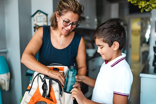 Mother helping young son pack backpack with water bottle