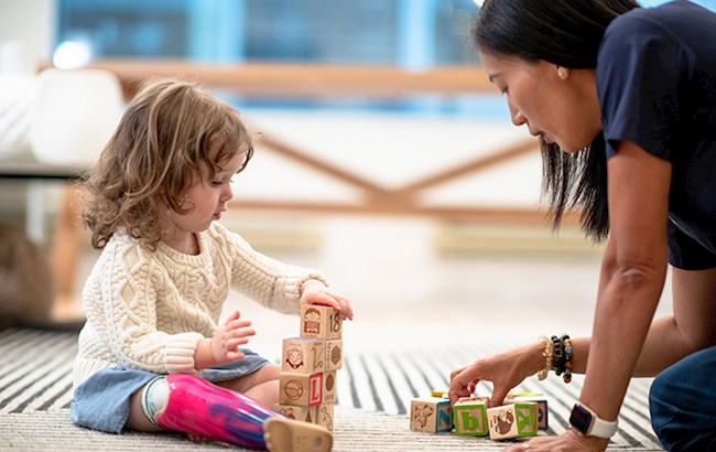Female occupational therapist sitting on floor with toddler with prosthetic leg playing with building blocks