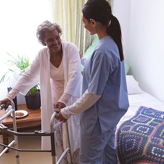 Female occupational therapist helping senior woman get out of bed and use walker