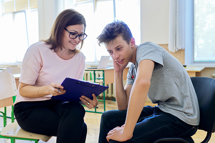 Woman talking with teenage boy in classroom both looking at tablet