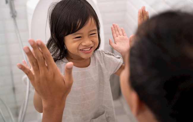 Toddler sits on toilet for potty training and gives adult a high five.