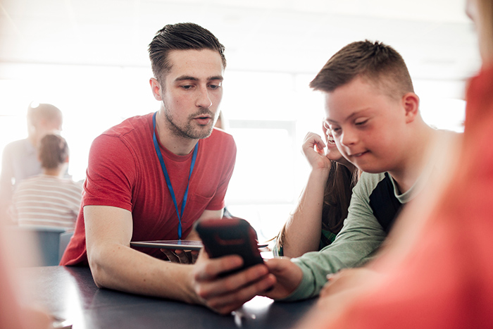 Man and teenage boy sitting at school table using tablet