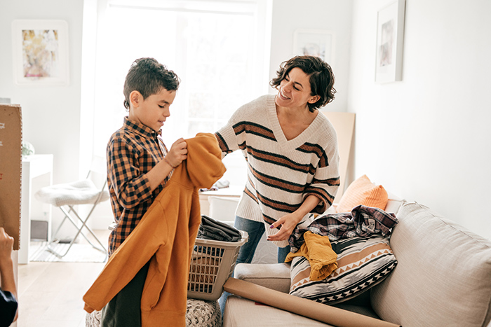 Woman at home with young boy folding clothes on couch