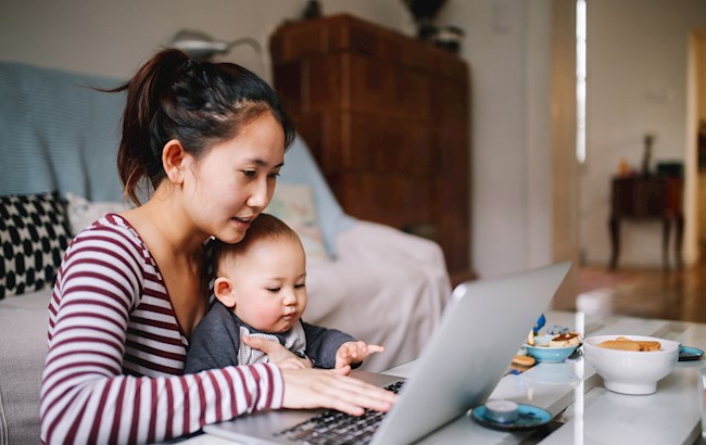 Parent sitting at a table with baby looking at a laptop