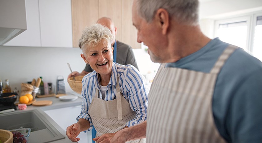 smiling senior woman and man with aprons in kitchen cooking