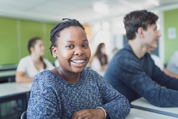Teenage girl sitting at desk in school next to classmates smiling