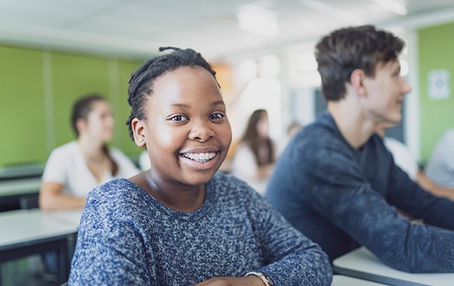 Teenage girl sitting at desk in school next to classmates smiling
