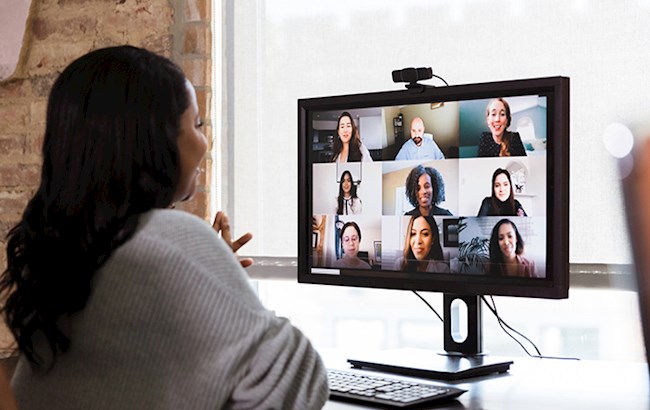 Woman sitting at desk looking at computer monitor talking to others on virtual meeting