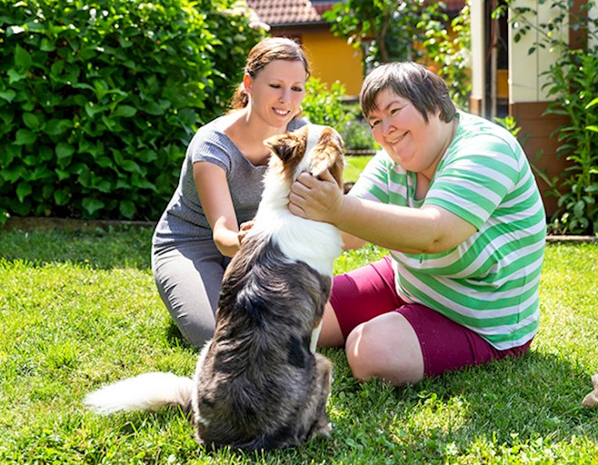 Two women sitting in grass outside petting a dog
