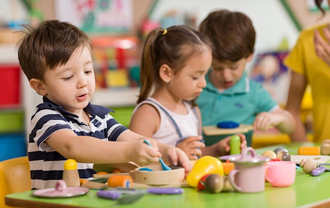 Three preschool aged kids sitting at classroom table playing with various toys