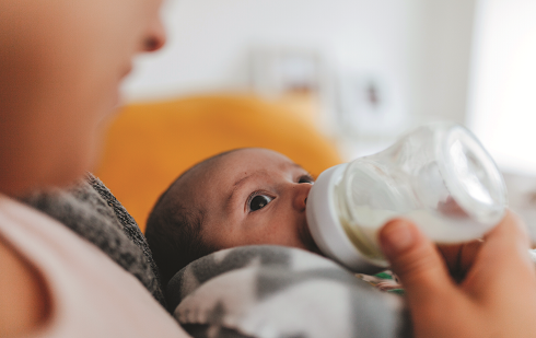 Person holding and feeding infant with a bottle.