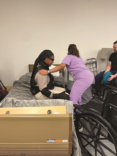 OT students engaging in bed mobility and functional transfers using geriatric simulation equipment to practice patient handling techniques.