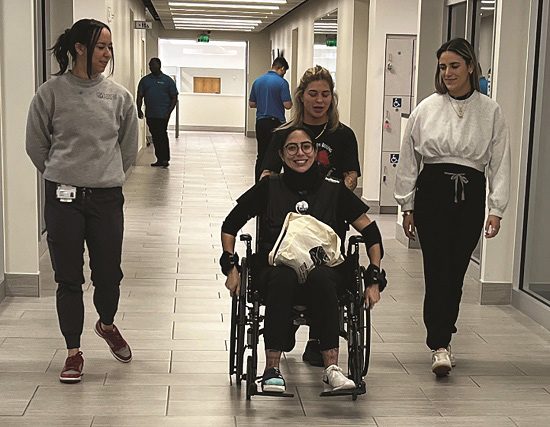 OT students participating in a wheelchair mobility exercise, navigating through a hallway to better understand accessibility challenges and improve their skills in assisting wheelchair users.