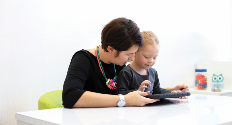 Teacher sitting with young student at a table looking at a tablet