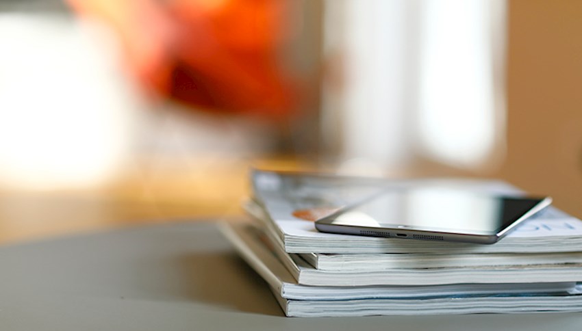 Stack of magazines on desk with eReader on top