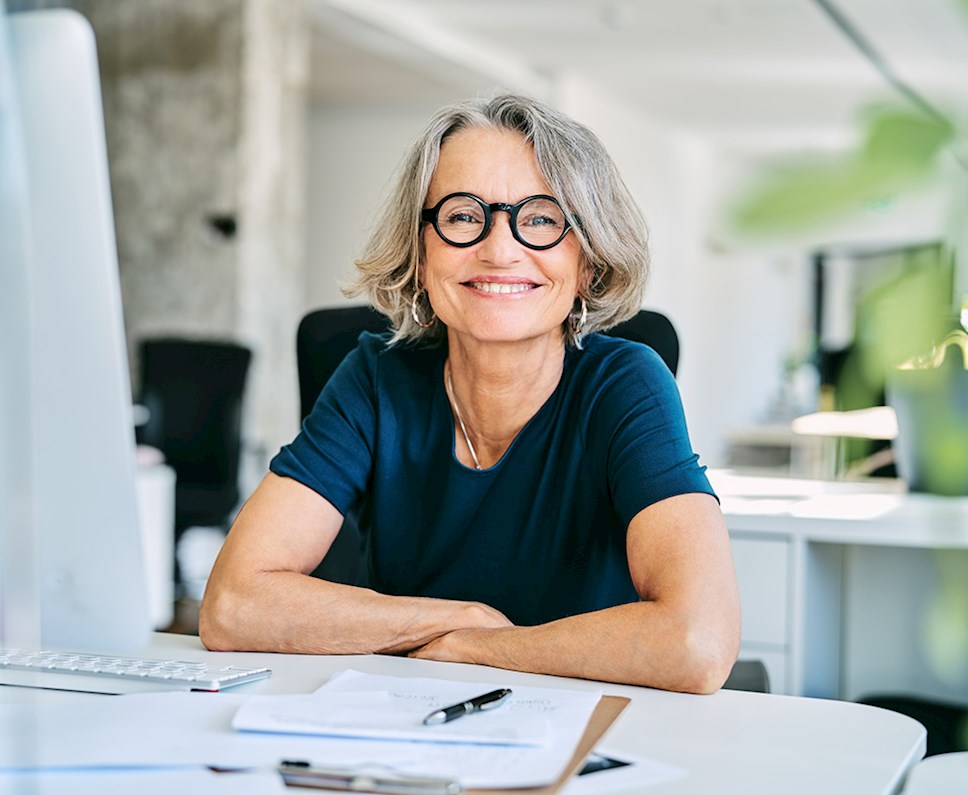 Mature woman smiling at desk while doing documentation paperwork
