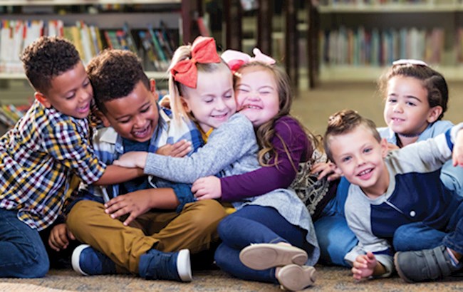 Group of children sitting in a library setting, smiling and hugging