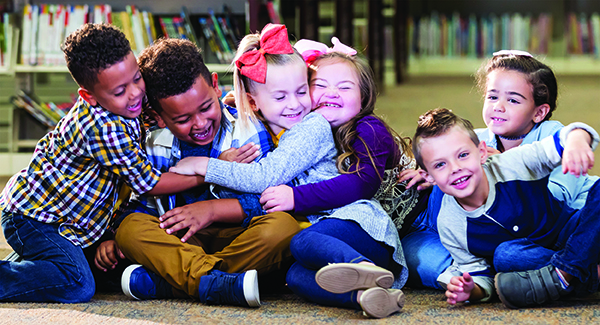 Group of children sitting in a library setting, smiling and hugging