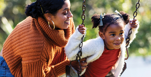 Woman smiling, pushing her child on a swing