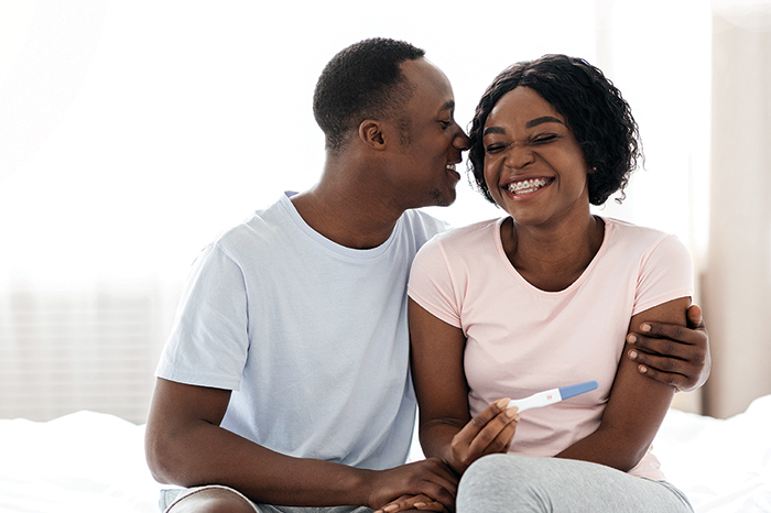 Man sitting beside woman holding positive pregnancy test while smiling.