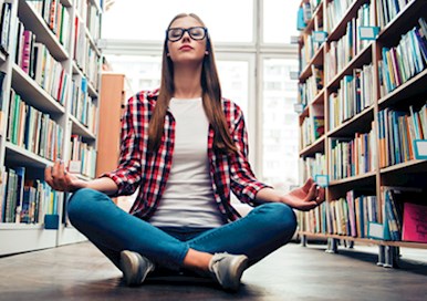 Woman sitting on floor between large bookcases with eyes closed and legs crossed.