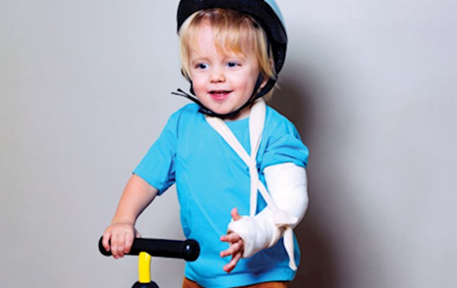 Toddler wearing a helmet with a casted arm in sling riding a tricycle